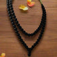 Black beaded necklace with a butterfly pendant on a wooden surface with flowers.