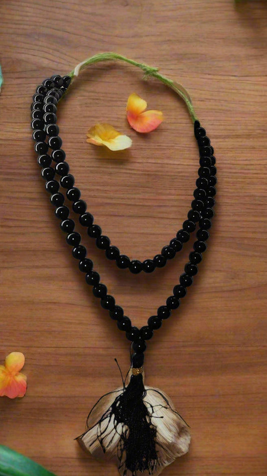 Black beaded necklace with a butterfly pendant on a wooden surface with flowers.